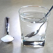 Glass of water with a spoon next to a tablespoon of salt