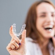 Woman laughing blurry in background holding Invisalign to foreground