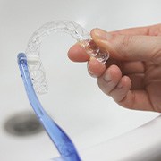 Hands brushing clear aligner at sink
