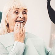 A senior woman looking at her dentures in a hand mirror