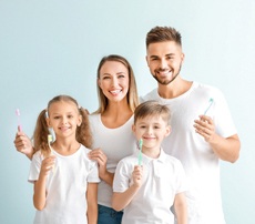 A husband and wife and their two children all holding toothbrushes and smiling after seeing their family dentist in Los Alamitos