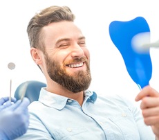 A young man with a beard looking at his smile in the mirror after a regular dental checkup and cleaning