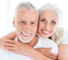 An elderly couple hugging and smiling after receiving restorative treatment