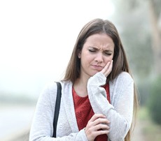 A young female holding her cheek in pain because of the effects of TMJ
