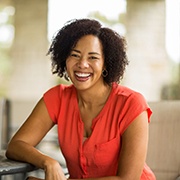 Woman in orange shirt smiling while sitting at a table outside