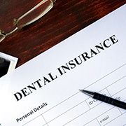 Photo of dental insurance form, pen, glasses, x-rays, and money on desk