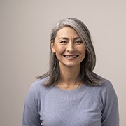 Woman with grey hair and grey shirt smiling with grey background