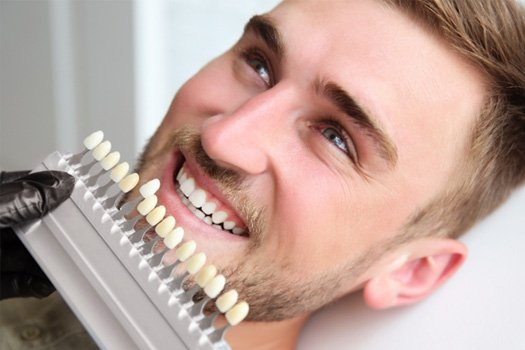 Man smiling with shade guide held to teeth