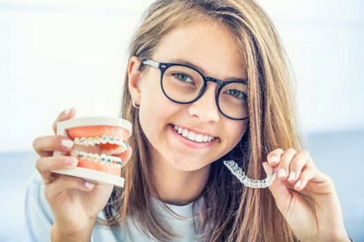 Girl holding model teeth with colorful braces in one hand and Invisalign in the other