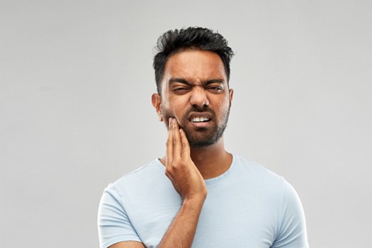 Man squinting and holding his hand to his jaw in pain