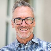 Man with grey hair smiling while wearing glasses