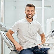 Man in grey collared polo and jeans smiling in dental chair