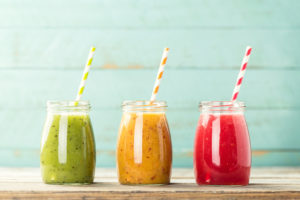 Three colorful fruit smoothies with straws on a ledge